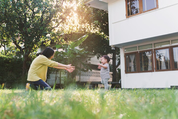 Portrait of Happy Chinese young Mother and her lovely Son relaxing playing and laughing at the garden of the house together.
