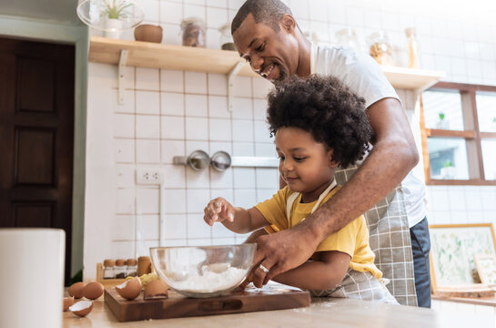 Smiling African American Father and little son while cooking in kitchen. Black family have fun while baking at home