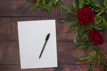 Hoja de papel blanco y pluma en mesa con flores y rosas rojas