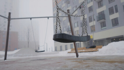Swing on background of houses in fog. Action. Empty swing eerily seesaw on background of fog. Empty...