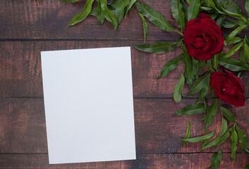 Hoja en blanco en mesa de madera con hojas verdes y rosas rojas