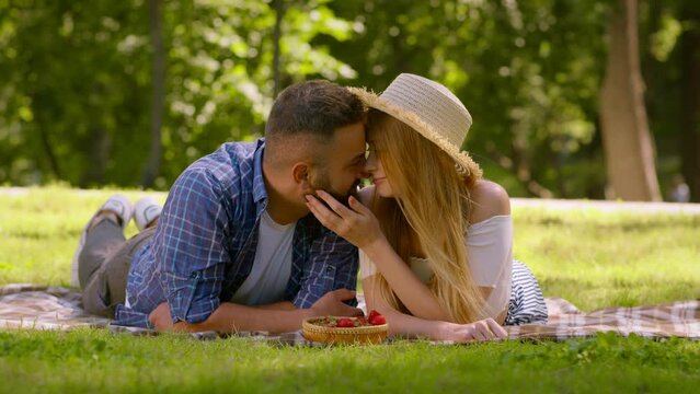 Love and tenderness concept. Happy loving man and woman resting on green grass in summer park, kissing each other