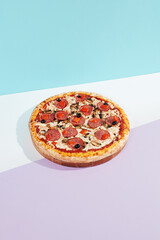Italian pizza with salami, mushroom, black olives on coloured background. Meat pizza with salami and olives minimal style on blue and purple color. American pizza delivery concept with color backdrop