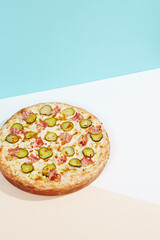 Italian pizza with bacon, pickled cucumber and crispy onion on coloured background. Homemade pizza in minimal style on blue and orange color. American pizza delivery concept with color backdrop.