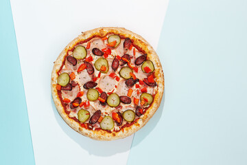 Italian pizza with sausage, jalapeno, ham and paprika on coloured background. Spicy pizza with jalapeno in minimal style on blue and orange color. American pizza delivery concept with color backdrop.
