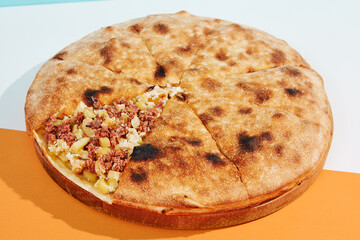 Closed pizza with minced meat, potatoes and cheese on coloured background. Meat pie with potatoes and cheese in minimal style. American pizza delivery concept with color backdrop.