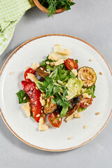 Salad with grilled vegetables, greens and cheese on concrete background. Warm salad with paprika, zucchini, eggplant and tomato on grill. Aesthetic composition with veggie salad. Summer menu concept.