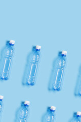 Pattern with blue plastic bottles on blue paper background, top view empty plastic bottle for water half litre, minimal image. Pollution, plastic garbage, environmental protection concept
