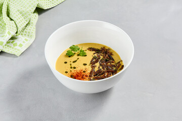 Cream soup with vegetables and crispy meat. Pea cream soup with spices on concrete background. Aesthetic composition with vegetables soup in white ceramic bowl