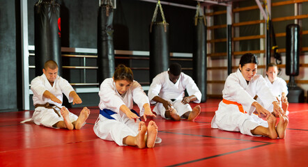 Group of men and women in kimono stretching on floor during karate training.