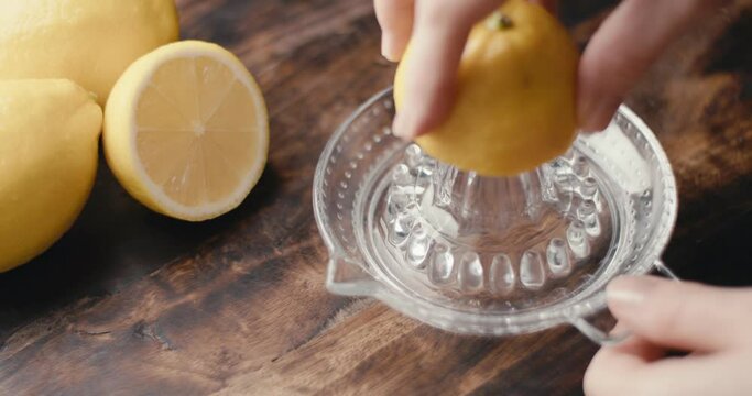 Hand squeezes lemon on glass squeezer juice in close up slow motion