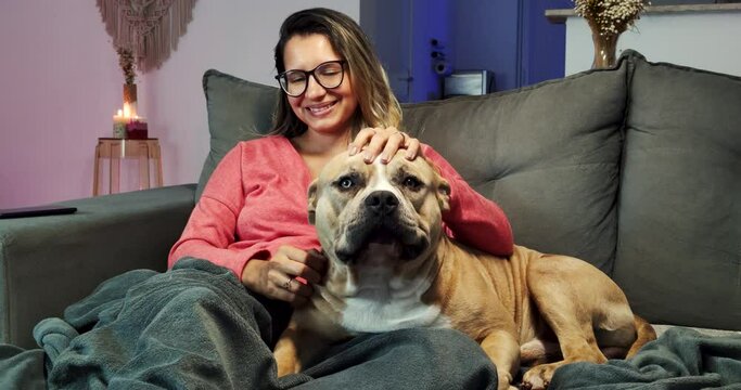 Jovem mulher sentada no sof&aacute; fazendo carinho no cachorro de grande porte