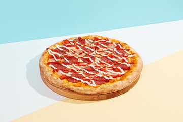 Italian pizza with ham and salami on coloured background. Meat pizza with ham, ketchup and mayonnaise in minimal style on blue colour. American pizza delivery concept with color backdrop