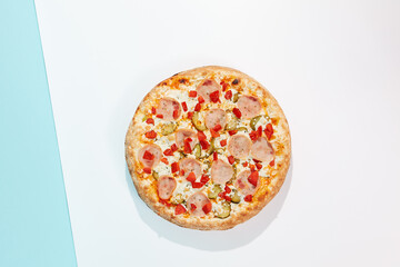 Italian pizza with ham and pickled cucumber on coloured background. Meat pizza with ham and vegetables in minimal style on light blue color. American pizza delivery concept with color backdrop