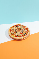 Italian pizza with mushroom and cheese on coloured background. Vegan pizza with mushroom and tomato in minimal style on blue and orange color. American pizza delivery concept with color backdrop