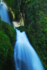 Naklejka premium Blue two stage waterfall flowing down a green mountain