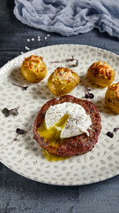 American breakfast - beefsteak with egg and roasted baby potatoes. Beef cutlet with poached egg in and potatoes in plate on stone background. Egg yolk on beef steak. Main course on meat.