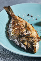 Grilled dorada in blue plate on stone background with textile. Roast fish in restaurant menu concept. Roasted whole dorado with lemon. Contemporary seafood menu. Mediterranean food.