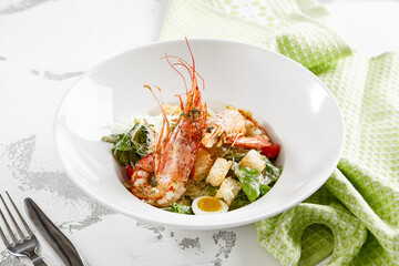 Classic Caesar salad with shrimps in white plate on stone table. Italian menu in restaurant. Seafood caesar on rustic style. Trendy salad with grilled prawns, green leaves, eggs, croutons and cheese. - obrazy, fototapety, plakaty