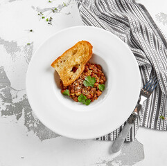 Georgian lobio in white plate with bread. Traditional georgian dish from red bean in sauce and spices.  Vegetarian appetizer from georgian cuisine. Caucasus lobio in restaurant menu. Vegan food.