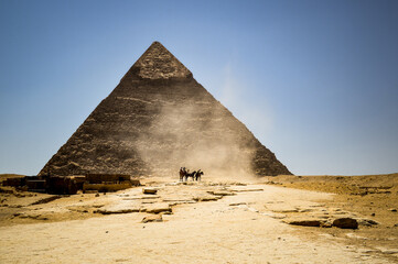Fototapeta na wymiar Horses and camels kick up dust in front of the Pyramid of Khafre at the Great Pyramids of Giza, Egypt.