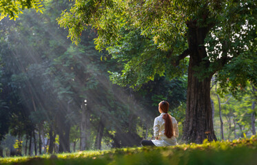 Back of woman relaxingly practicing meditation in the forest to attain happiness from inner peace...
