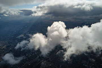 Aerial view from airplane window at high altitude of distant city covered with puffy cumulus clouds forming before rainstorm