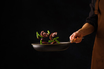 Octopuses with vegetables in a pan in a frozen flight in the hand of a professional chef on a black background. Sea Asian cuisine. Organic vegetarian food, gourmet food. Restaurant, hotel, banquet.