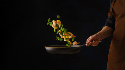 Shrimp with greens, vegetables and lemon slices in a pan in a frozen flight on a black background....