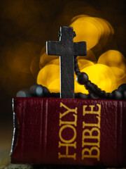 Catholic cross on a rosary on a book - the Holy Bible. Fantasy yellow background with twinkling...