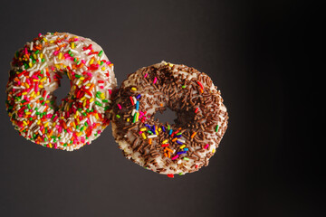 Two multi-colored sweet donuts on a gray background in a frozen flight. Sweet food, calories, fast...