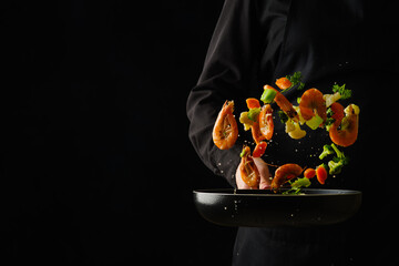 A bright assortment of shrimp, vegetables and greens in a frying pan in a frozen flight on a black...