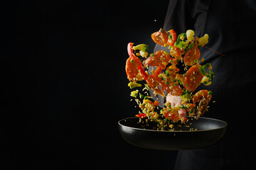 The process of cooking seafood with vegetables in a frying pan by a professional chef in a black uniform. Food in a frozen flight on a black background. Advertising, banner.