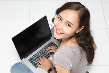 Beautiful Asian woman wearing grey casual shirt using laptop on white background and copy space. Cute Asian woman sitting on the floor room relaxing  for work from home concept