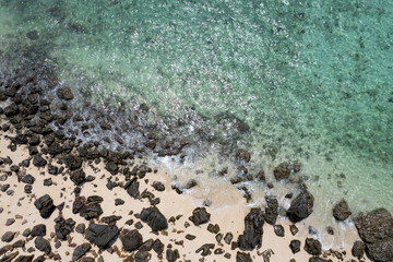 Aerial view of sea water blowing towards the beach. The beach has black rocks, contrasting with the sea sand. Amazing beauty.on the island of the Andaman Sea