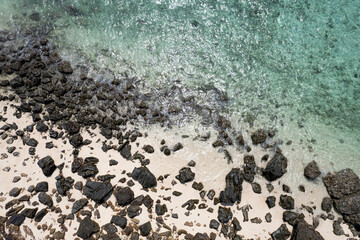 Aerial view of sea water blowing towards the beach. The beach has black rocks, contrasting with the sea sand. Amazing beauty.on the island of the Andaman Sea