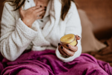 latin adult woman with balsam, ointment or holding jar of cream for flu on bed at home in Mexico...