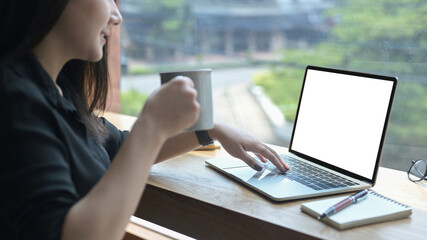 Young woman drinking coffee and using laptop computer. Empty screen for advertising text.