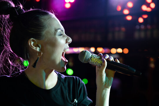 Young Singing Woman With Microphone Having Fun On Open Stage In Karaoke Club.