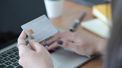 Close up view woman hand holding plastic credit card and using laptop. Online shopping, internet banking concept.