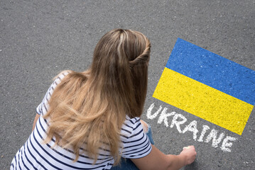 Eine junge Frau malt Flagge der Ukraine auf die Straße