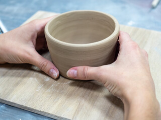 Close-up of women's hands holding a planter made of raw clay. Handmade, workshop, workshop. Selective focus