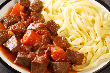 Slowly stewed spicy beef in red wine with vegetables served with noodles close-up in a plate on the table. horizontal