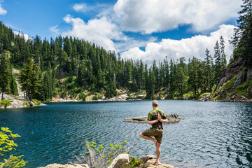 Fototapeta na wymiar Adventurous male hiker doing a yoga pose on the shore of an alpine lake in the Pacific Northwest.