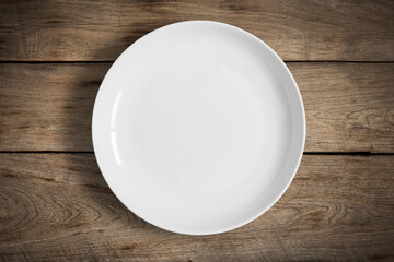 Top view of blank white food plate on a wood background with copy space.