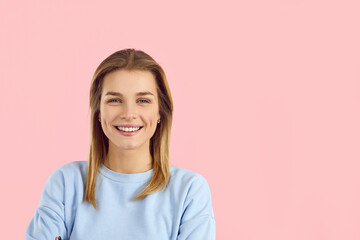 Studio shot of beautiful young caucasian woman looking at camera with charming cute smile. Close up of blonde girl in light blue sweatshirt isolated on pink background. Banner. Isolated. Copy space.