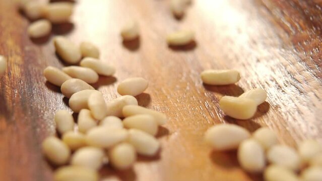Fresh peeled siberian pine nuts. Raw hulled cedar seeds falling on a textured surface of rustic wooden surface. Shelled kernels. Macro. Rotation. Slow motion