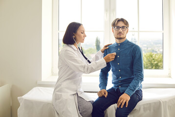Female doctor with stethoscope listening to young man's heartbeat. Woman who works as physician...