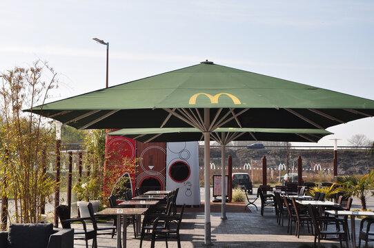 Mc Donald`s Gastronomie: Der Außenbereich von der Fastfood Burgerkette,  viele Tische und Stühle für die Gäste auf der Terasse mit Sonnenschirm