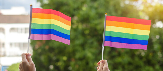 hands showing LGBTQ Rainbow flag on green nature background. Support Lesbian, Gay, Bisexual, Transgender and Queer community and Pride month concept